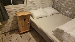 Un petit meuble en bois avec une découpe en forme de cœur, un lit simple avec une literie blanche et une fenêtre avec des stores.