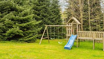 Un parque infantil con columpios y tobogán, rodeado de árboles frondosos.