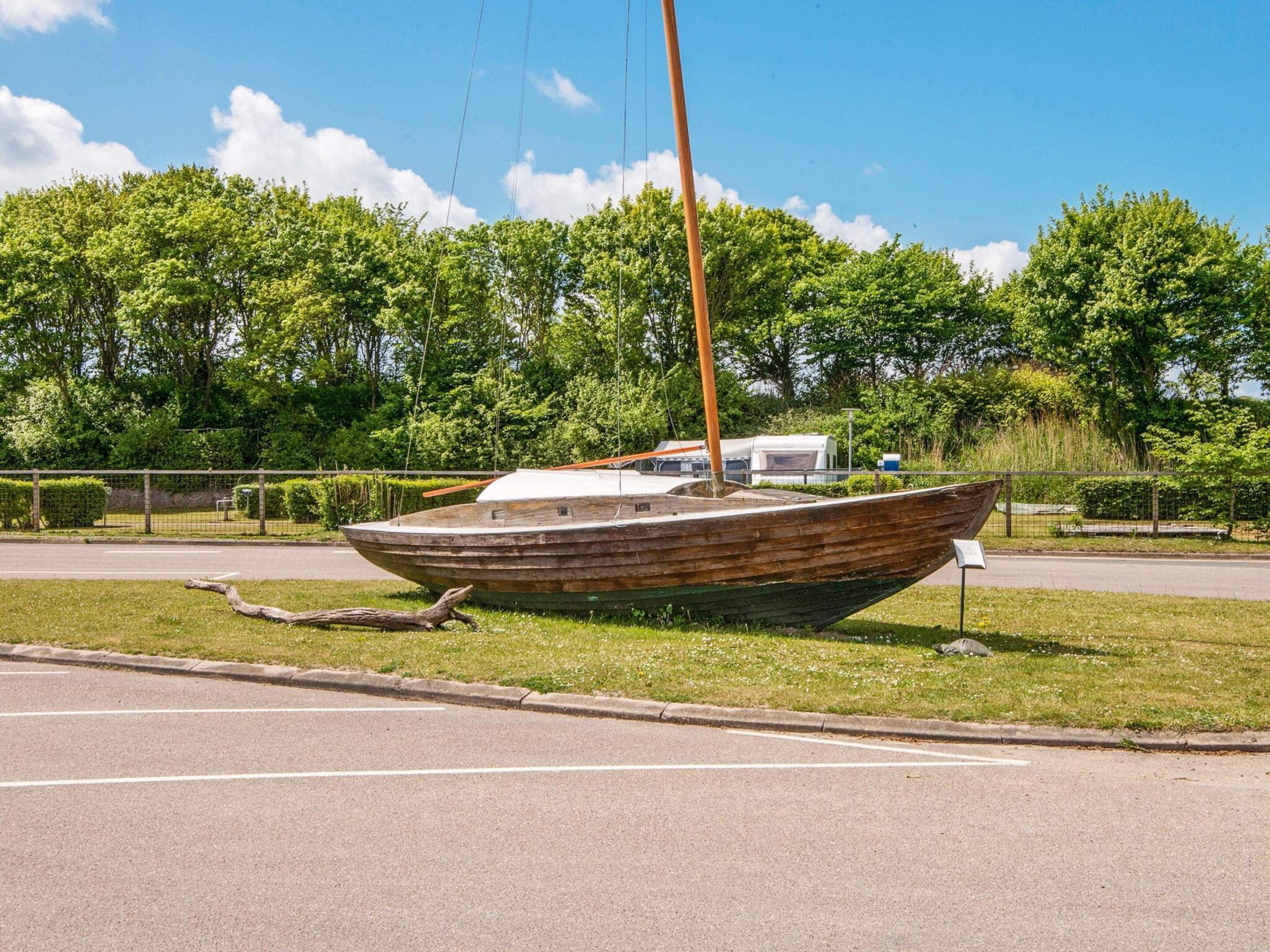 Un bateau en bois, doté d’un mât, est posé sur l’herbe, au bord d’une route.