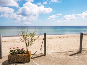 A beach with a concrete planter containing plants and flowers, a wooden fence, and a clear view of the ocean. - Holiday Home in Sydals (Sydals)