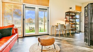 A modern living room with a red sofa, a wicker ottoman, and a dining area with a table and chairs. - Holiday Home in Tripscompagnie Near Nature (Tripscompagnie)
