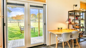 A dining area with a table and chairs, a bookshelf, and a view of a grassy outdoor area through glass doors. - Holiday Home in Tripscompagnie Near Nature (Tripscompagnie)