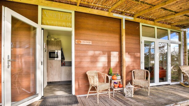 A wooden exterior with a covered porch, wicker chairs, a small table with a potted plant, and a sign reading "Hotchkiss." - Holiday Home in Tripscompagnie Near Nature (Tripscompagnie)