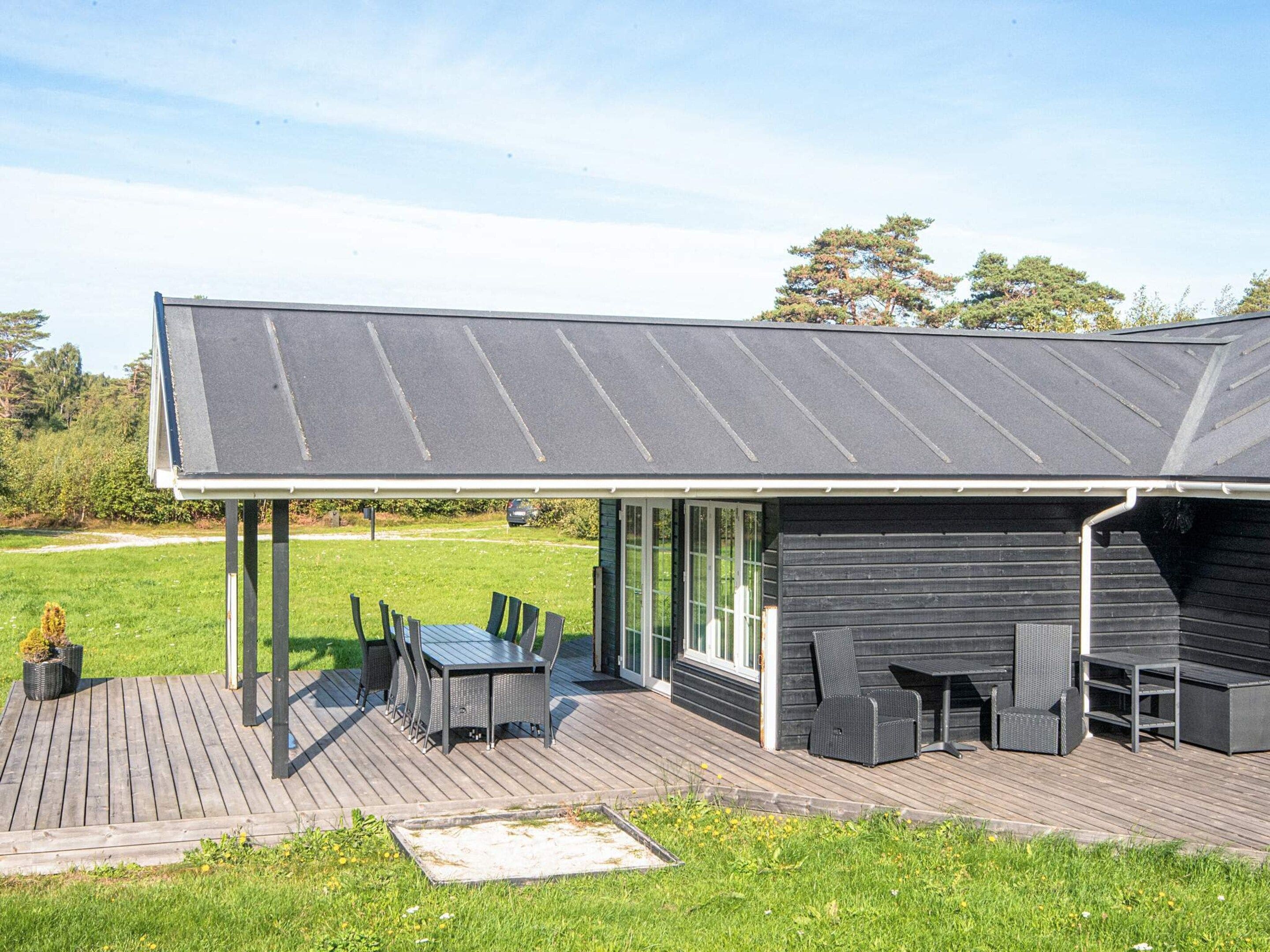 A covered outdoor area with a table and chairs, a wooden deck, and a building with a dark exterior.