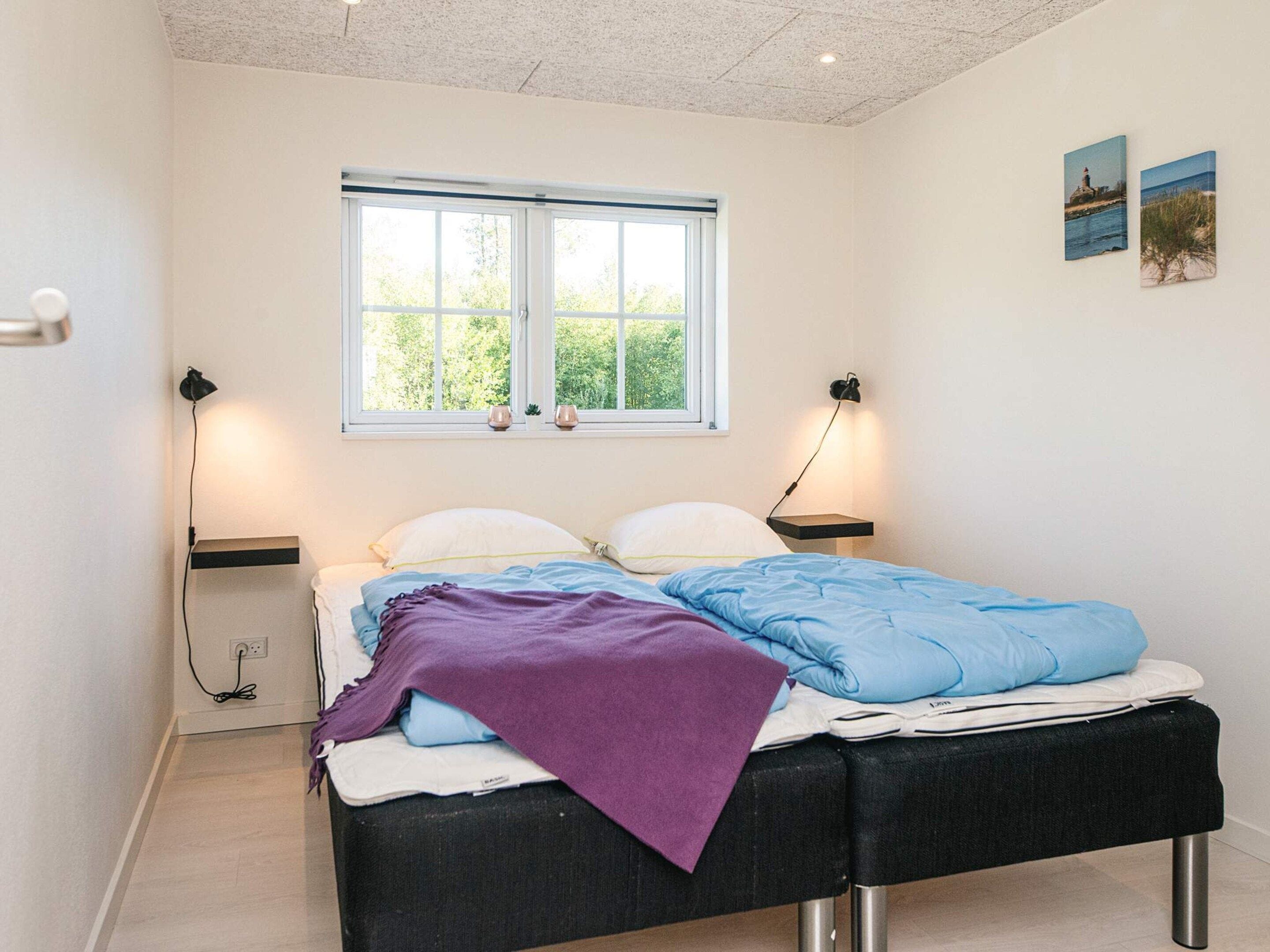 Un dormitorio con cama, lámparas de noche, ventana y una obra de arte en la pared.