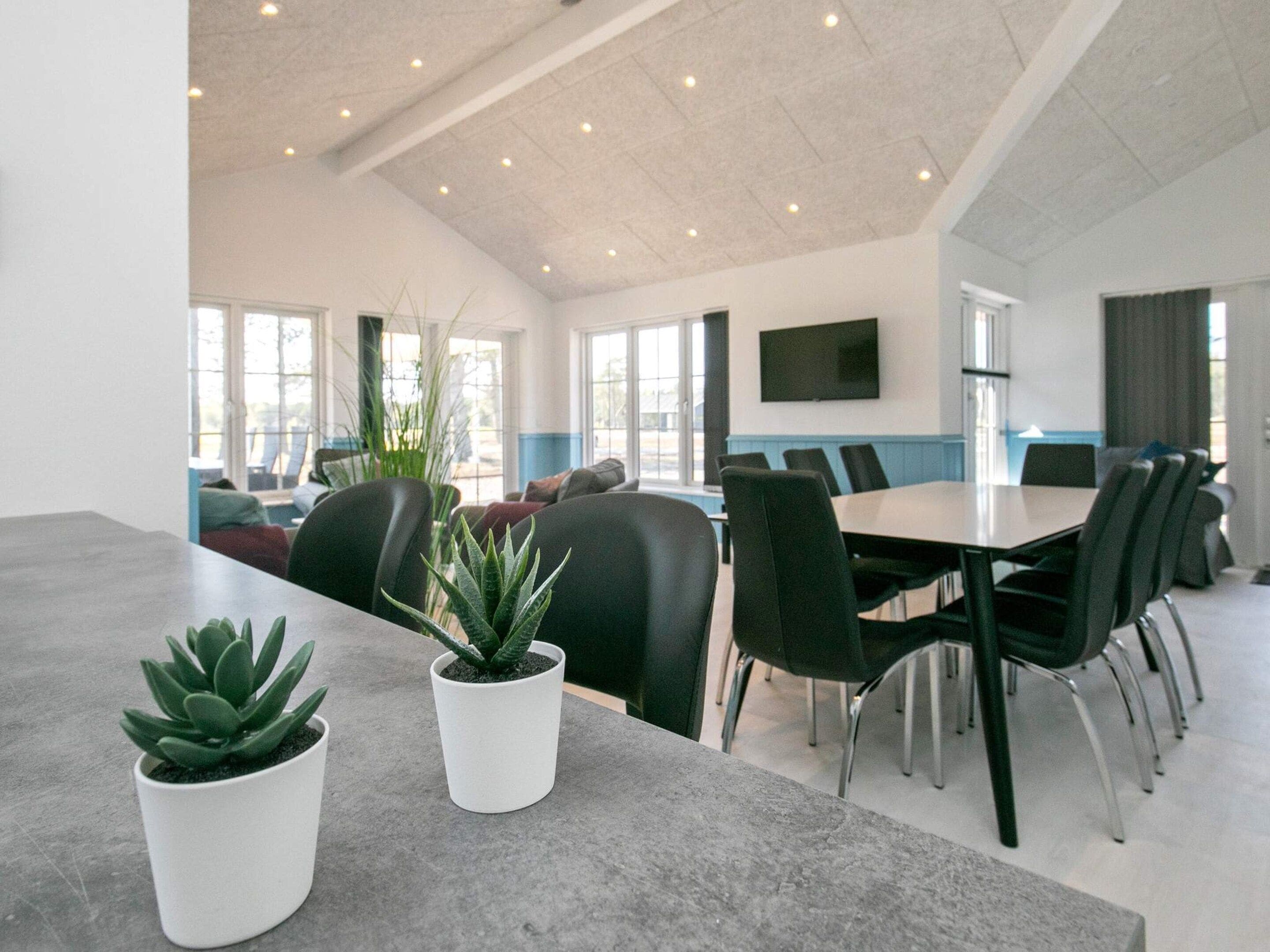 A spacious conference room with a long table, black chairs, and potted plants.