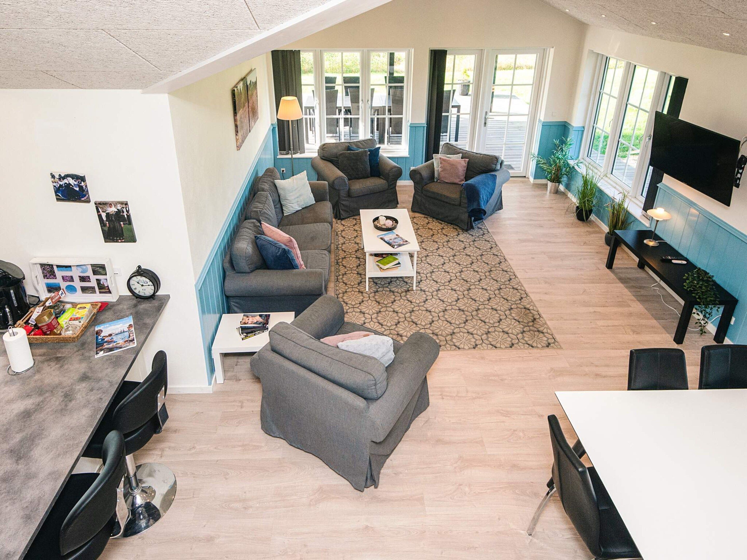 A spacious living area with multiple sofas, a coffee table, and a dining table. There are large windows providing natural light and a view of the outdoors.