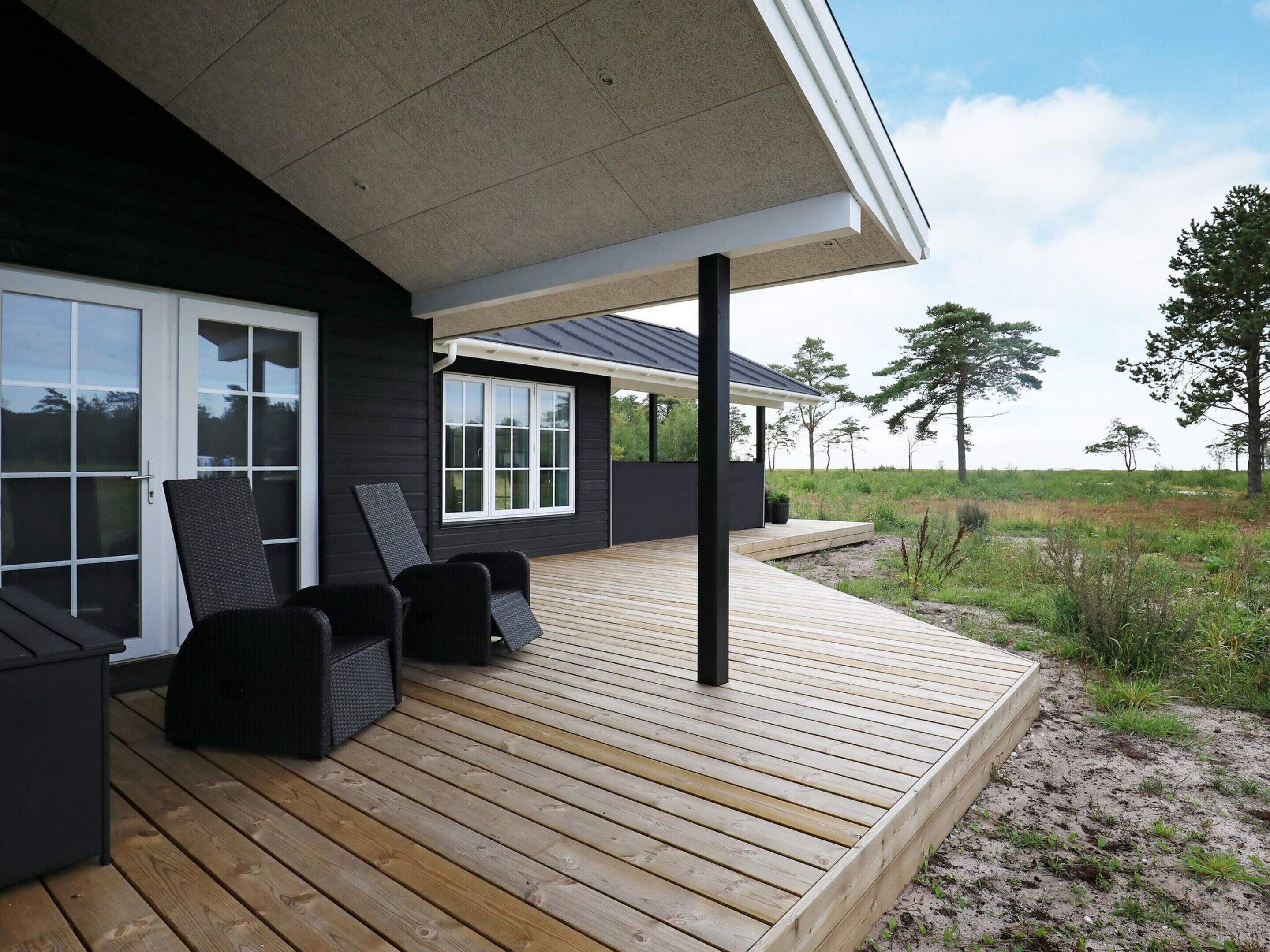 Una casa moderna con terraza de madera, paredes exteriores negras y ventanas amplias.