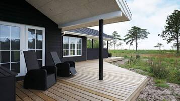 Una casa moderna con terraza de madera, paredes exteriores negras y ventanas amplias.