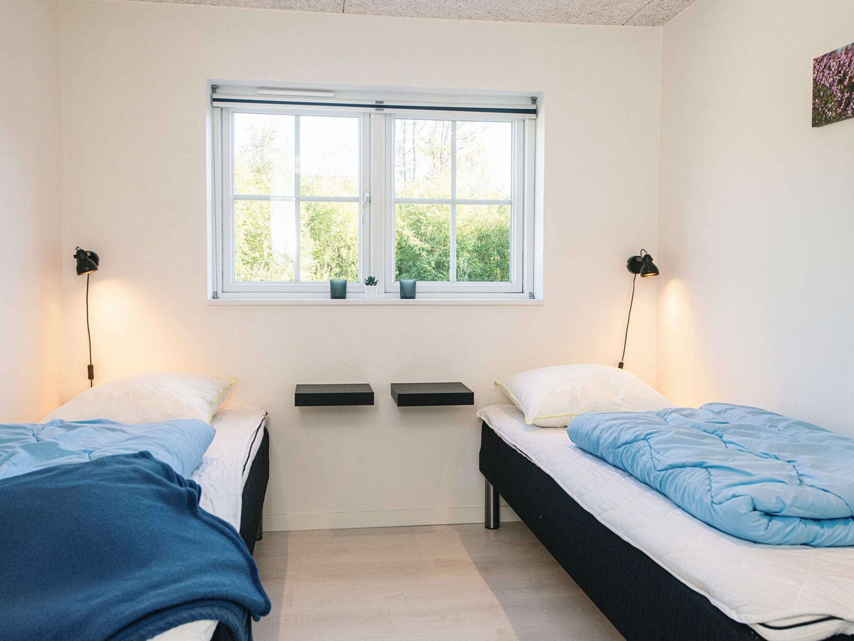 Habitación con dos camas, una ventana y dos lámparas fijadas a la pared.