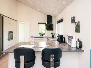 A modern kitchen with a central island, built-in oven, and a window with blinds.