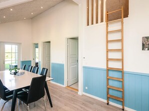 A dining area with a long table and chairs, a wooden ladder against the wall, and doors leading to other rooms.