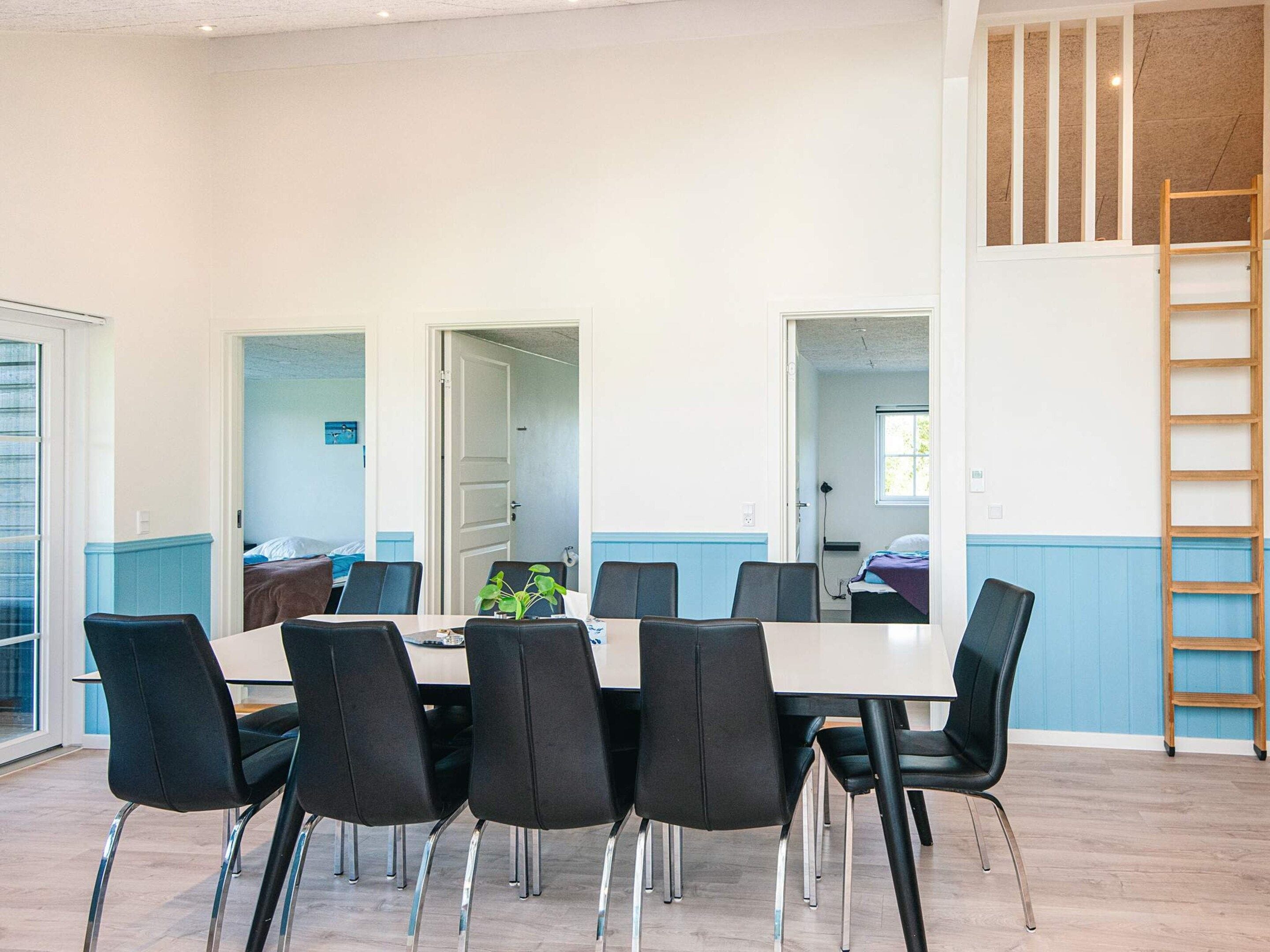 Un comedor moderno con una mesa rectangular y seis sillas, una escalera de madera y vista a un dormitorio a través de una puerta abierta.