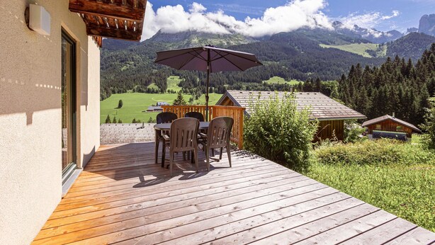 Une terrasse en bois avec une table et des chaises, offrant une vue sur un paysage montagneux.