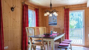 Un intérieur en bois comprenant une table à manger, des chaises, un lustre et une vue sur l’extérieur.