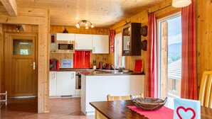 L’intérieur d’un chalet en bois comprend une cuisine, un coin repas et une grande fenêtre agrémentée de rideaux.