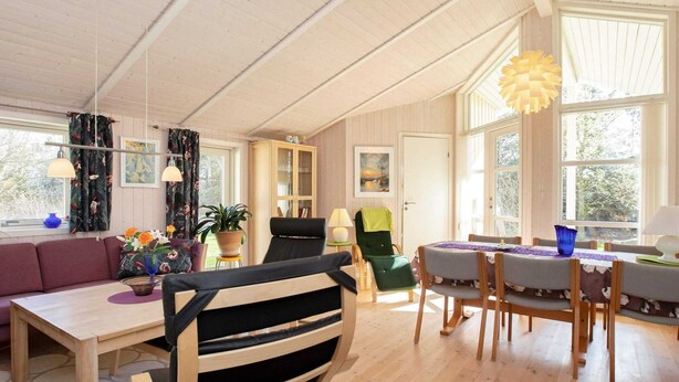 A spacious living room with a wooden floor, a dining area with a table and chairs, a sofa, a chair, and a bookshelf. - 6 Person Holiday Home in Gilleleje-by Traum (Gilleleje)