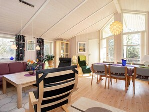 A spacious living room with a wooden floor, a dining area with a table and chairs, a sofa, a chair, and a bookshelf.
