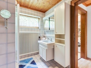 A modern bathroom with a shower, a sink, and a toilet. There is a window with a lace curtain and a radiator on the wall. - Apartment Near the Koralpe ski Area (Frantschach-Sankt Gertraud)