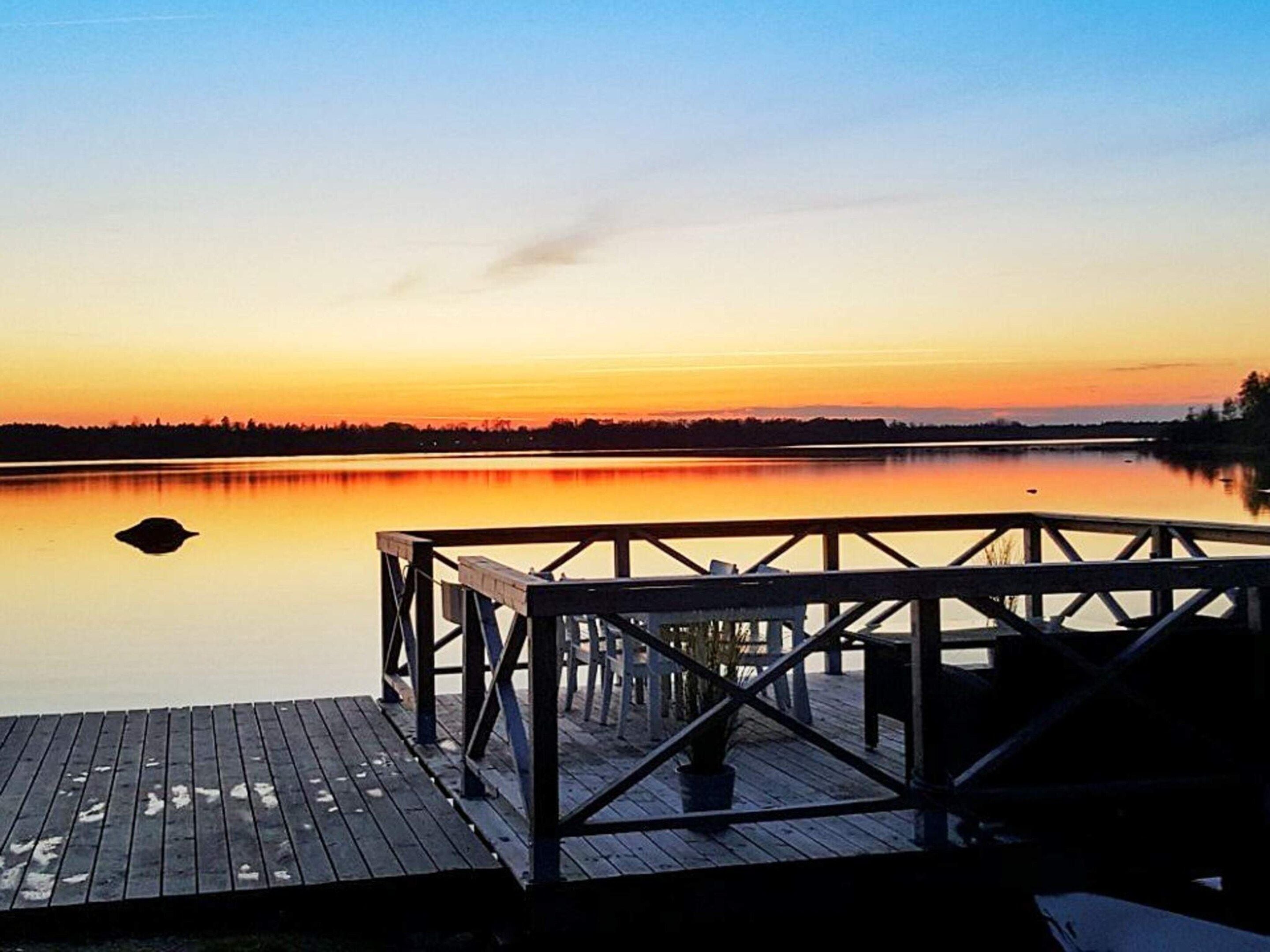 A wooden dock extending into calm water with a sunset in the background.