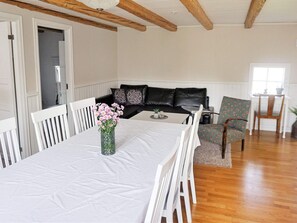 A dining area with a table set for four, a vase with flowers, and a black leather sofa with patterned cushions. - 4 Person Holiday Home in Vackelsang (Väckelsång)