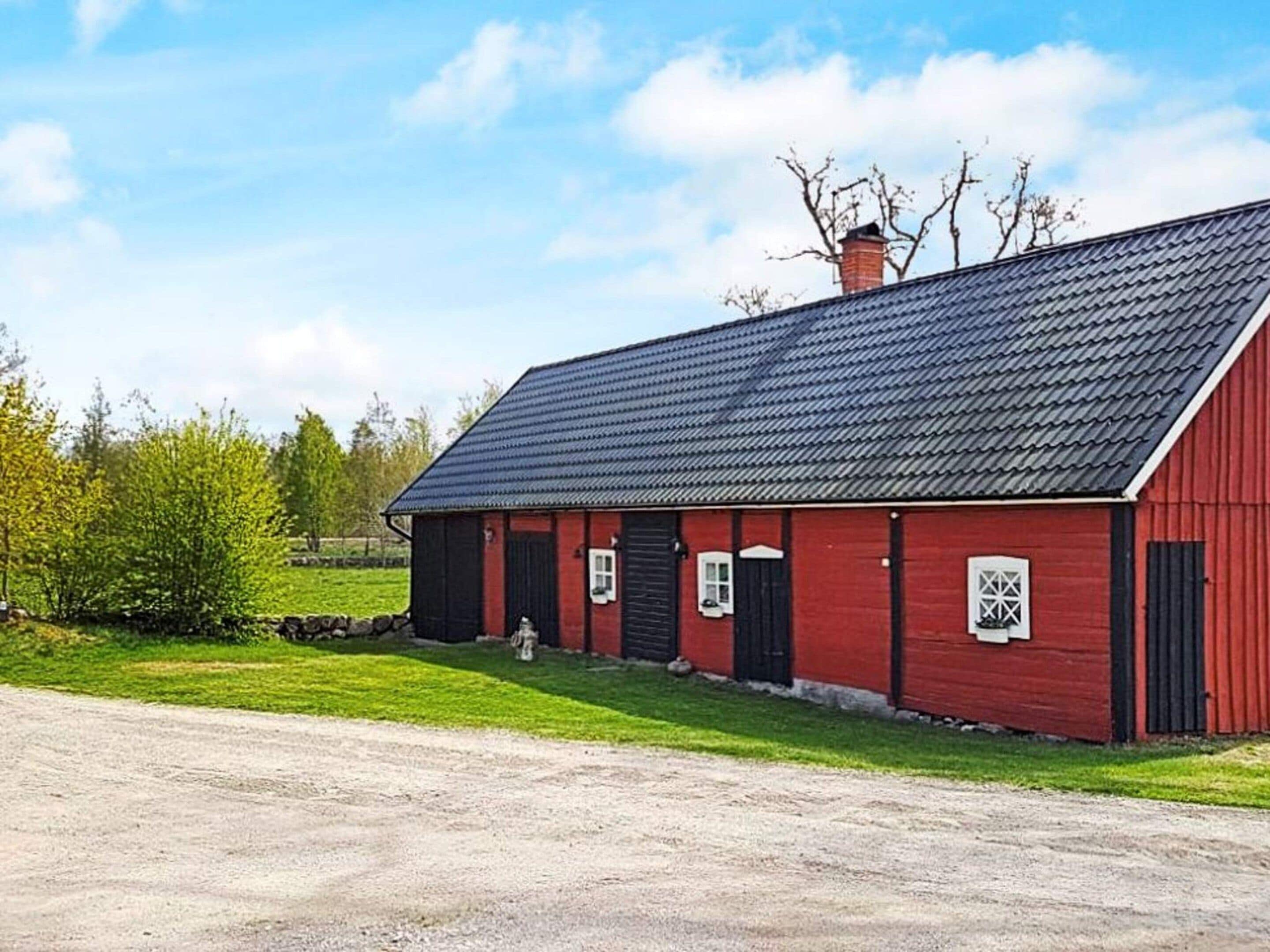 Ein rotes Bauernhaus mit dunklem Dach, einer Steinsäule und einer grünen Wiese davor.