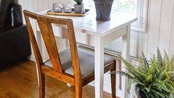 A wooden chair with a cushioned seat and backrest, a white table with a tray holding a potted plant and two decorative items, and a large potted fern plant to the side.