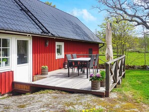 A red wooden house with a black roof, a deck with outdoor furniture, and a garden. - 4 Person Holiday Home in Vackelsang (Väckelsång)