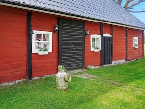 A red wooden building with a black door, two windows with white frames, and a small stone structure in front. - 4 Person Holiday Home in Vackelsang (Väckelsång)