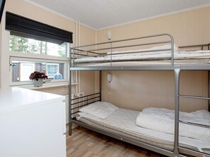 Une chambre avec un lit superposé, une fenêtre, une table de chevet et une plante en pot.