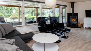 A modern living room with a sofa, two black leather chairs, a white round table, and a fireplace. - 6 Person Holiday Home in Vaeggerlose (Vaeggerlose)