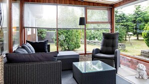 A sunroom with wicker furniture, large windows, and a view of the garden. - 6 Person Holiday Home in Vaeggerlose (Vaeggerlose)