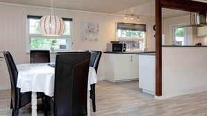 A dining area with a table and chairs, a kitchen with a microwave, and a window with blinds. - 6 Person Holiday Home in Vaeggerlose (Vaeggerlose)