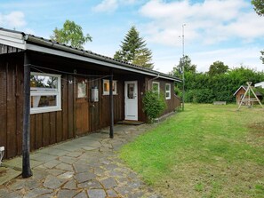 Une cabane en bois avec une entrée pavée de pierres, un petit porche et une cour clôturée.