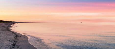 A beach with a calm sea, a clear sky, and a distant horizon.
