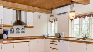 A kitchen with wooden cabinets, a stainless steel range hood, a dishwasher, and a window with a view of trees. - 12 Person Holiday Home in Hojer (Højer)