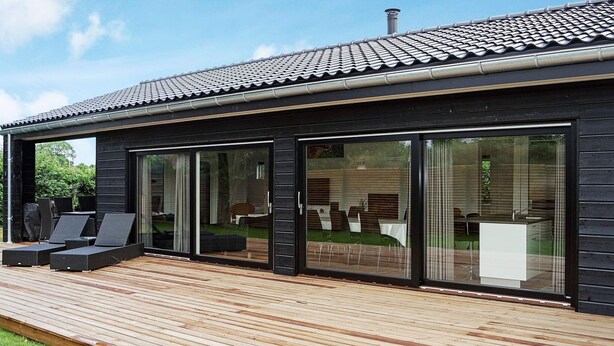 A modern house with a wooden deck and large sliding glass doors leading to an outdoor dining area. - Holiday Home in Hadsund (Hadsund)
