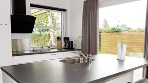 A modern kitchen with a large island, stainless steel appliances, and a window overlooking greenery. - Holiday Home in Hadsund (Hadsund)