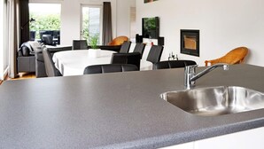 A modern kitchen with a stainless steel sink, a dining area with a table and chairs, and a view of the outdoors. - Holiday Home in Hadsund (Hadsund)