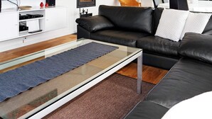 A modern living room with a black leather sofa, a glass coffee table, and a flat-screen TV on a white stand. - Holiday Home in Hadsund (Hadsund)