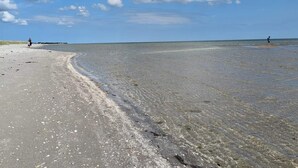 Une plage avec une eau claire et peu profonde, un rivage sablonneux et une jetée qui se dessine à l’horizon.