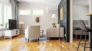 A modern living room with a sofa, armchair, and a TV. There is a wooden floor and a patterned wallpaper. - 4 Star Holiday Home in Loftahammar (Loftahammar)