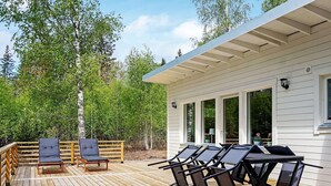 A wooden deck with outdoor seating, including lounge chairs and a table, adjacent to a white building with large windows. - 4 Star Holiday Home in Loftahammar (Loftahammar)