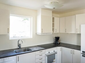 Ett modernt kök med vita skåp, en diskho i rostfritt stål, en inbyggd ugn och ett fönster som släpper in naturligt ljus.