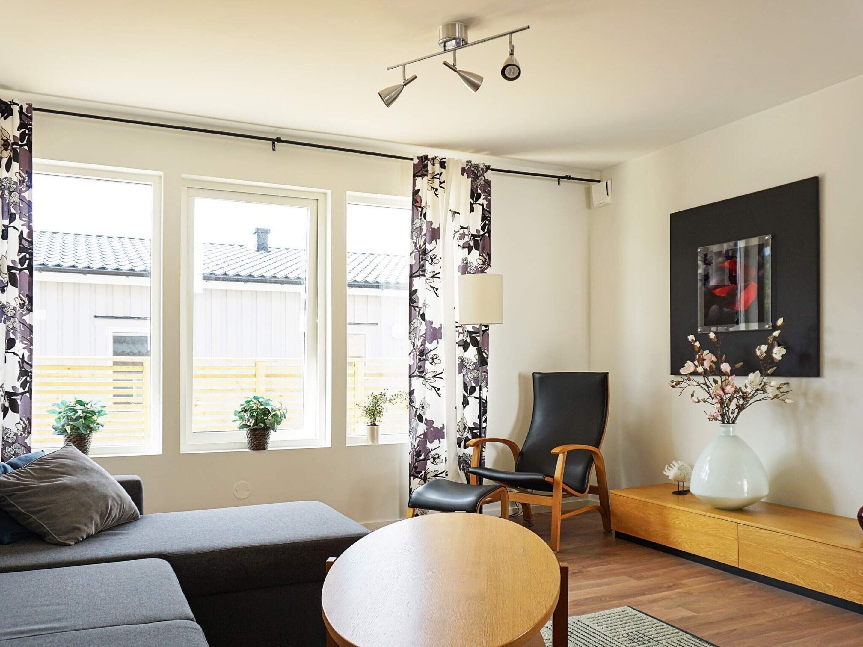 A modern living room with a sofa, chairs, a round table, and a potted plant.