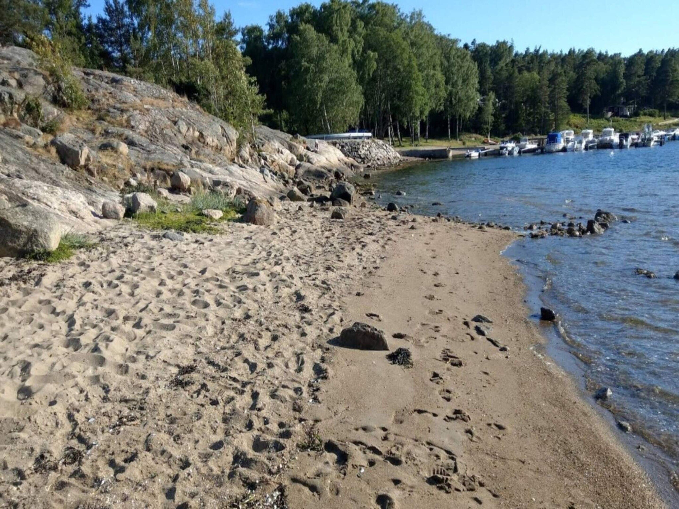A sandy beach with footprints, a rocky shoreline, and boats in the water.