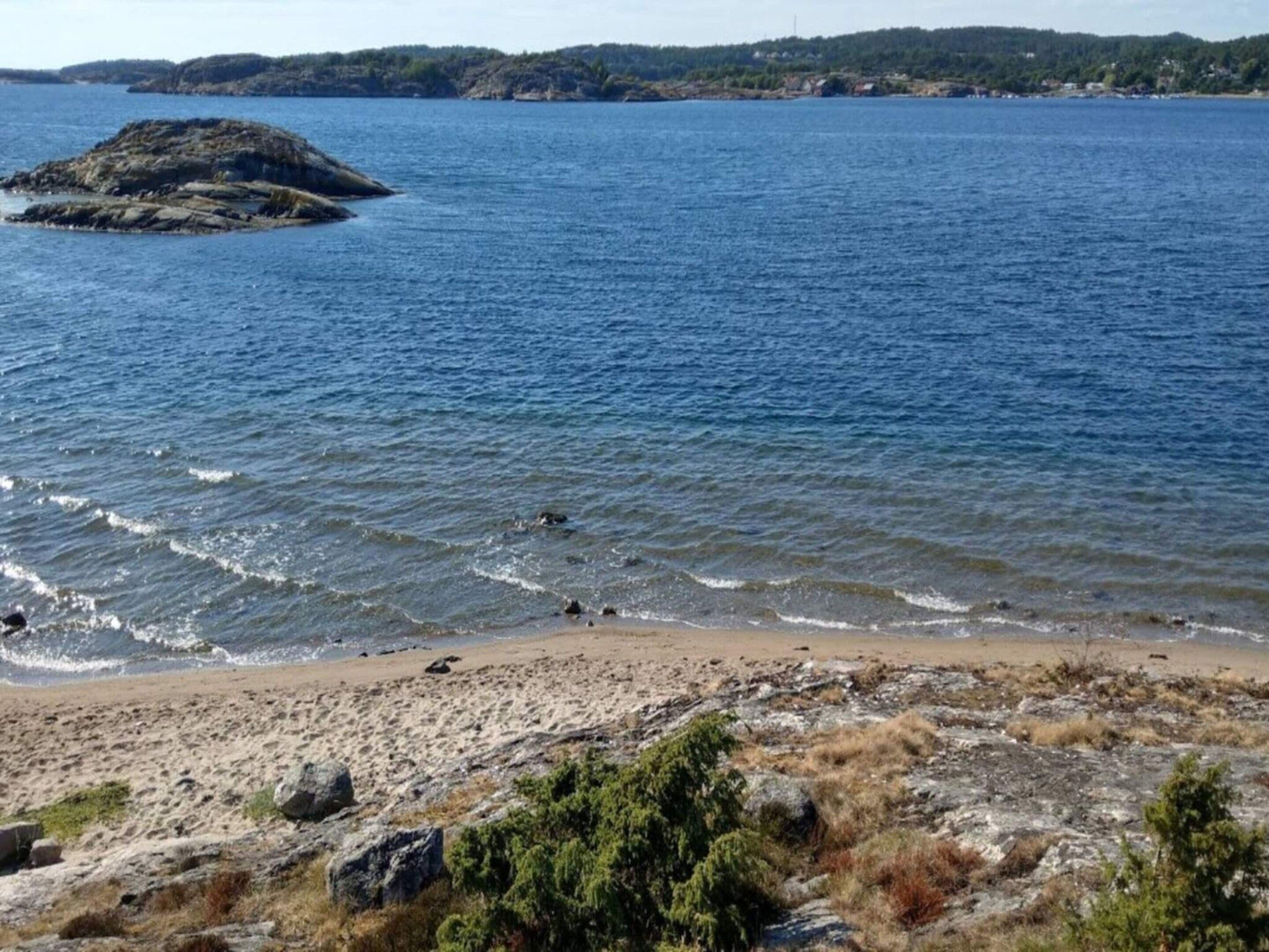 Paisagem costeira com falésias, mar calmo e colinas ao longe.