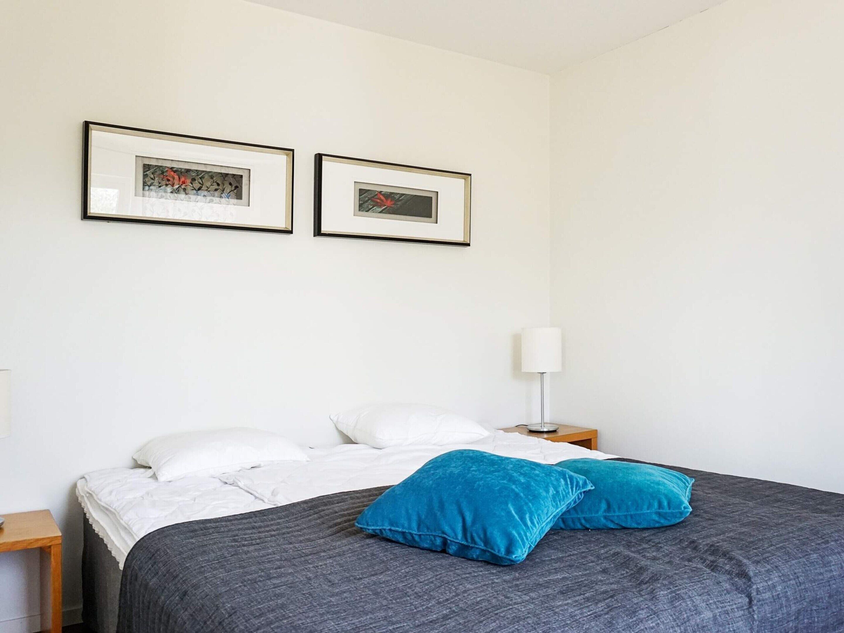A bedroom with a bed, two pillows, a nightstand, a lamp, and two framed pictures on the wall.