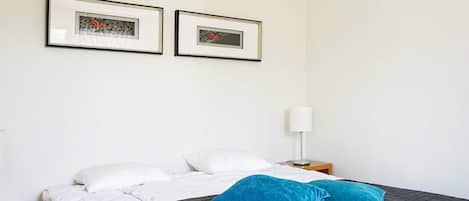 A bedroom with a bed, two pillows, a nightstand, a lamp, and two framed pictures on the wall.