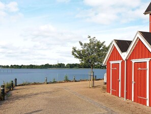 A gravel path leading to a red building with white trim, a tree, and a body of water in the background. - Holiday Home in Gravdal (Grasten)
